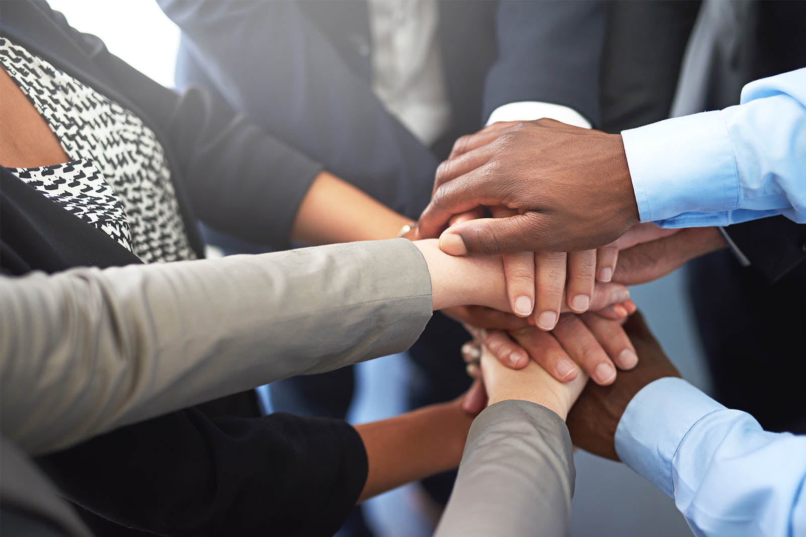 Several hands stacked together in center of group of people.