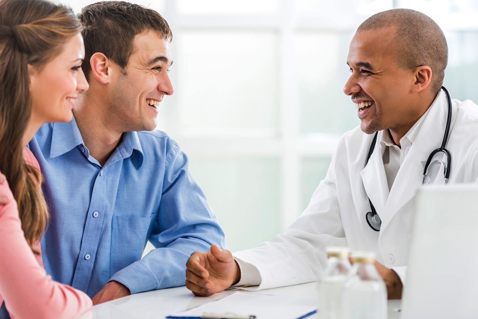A male doctor having conversation with patients, all smiling.