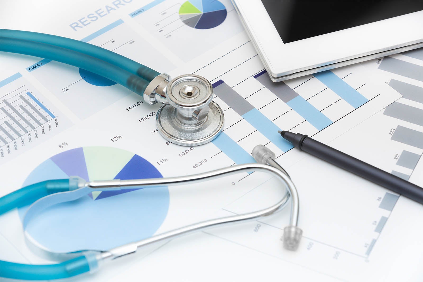 Charts, graphs, stethoscope, and laptop strewn on desktop.