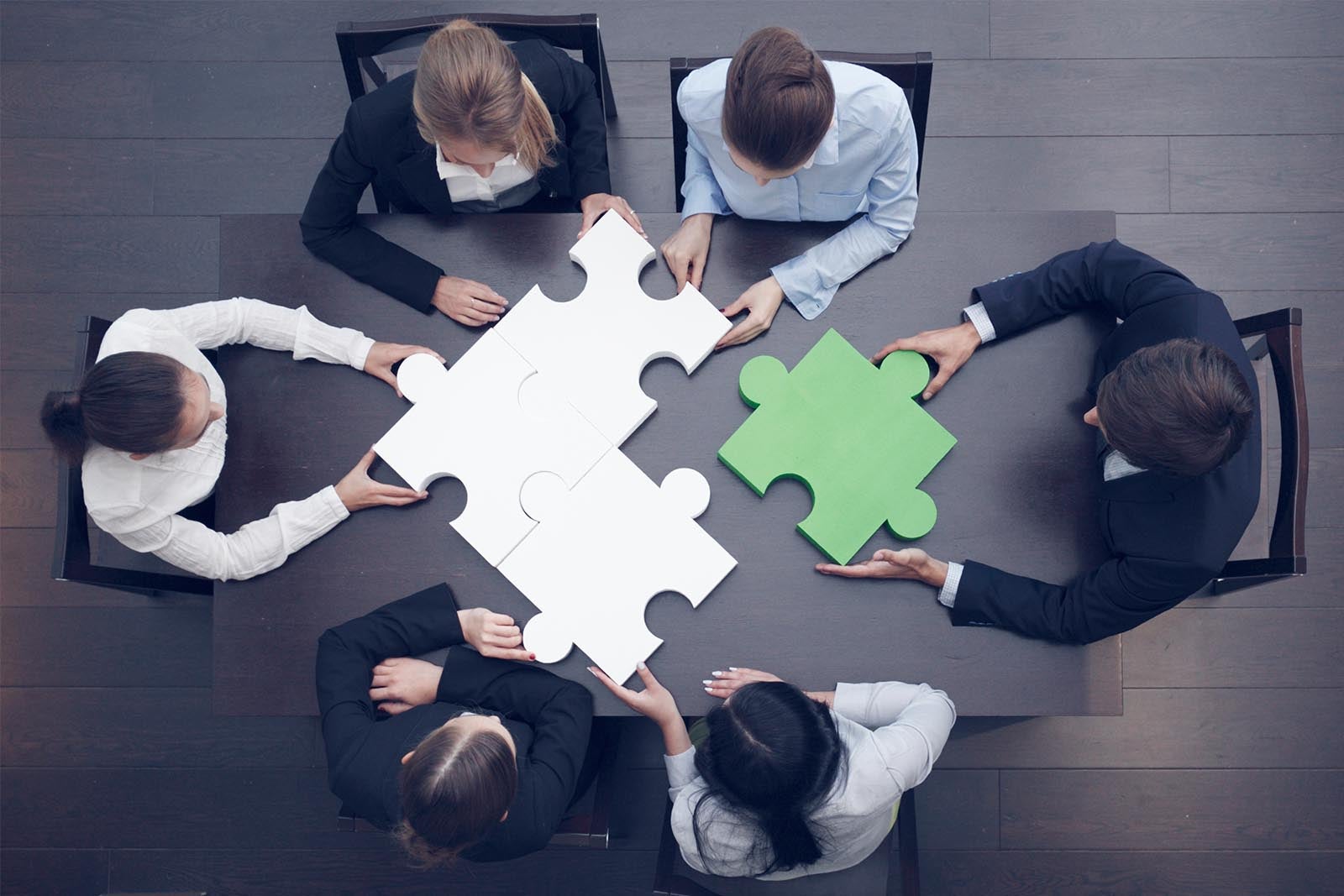 Group of business people putting together overly large puzzle pieces.