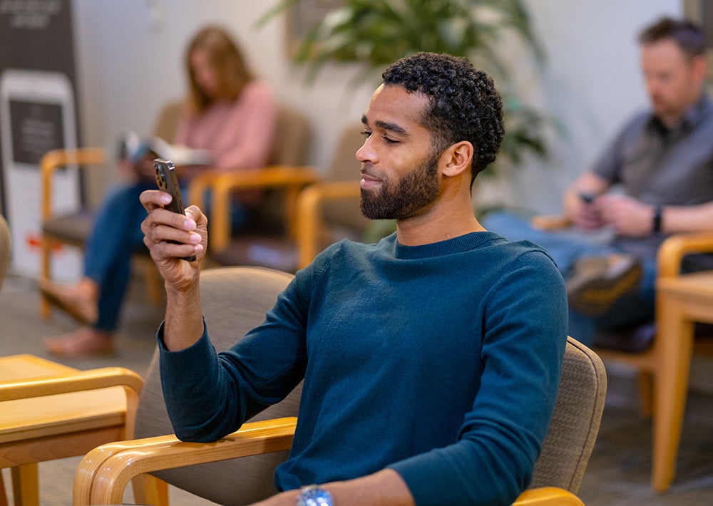 a patient in a waiting room using his mobile phone to complete the patient intake process