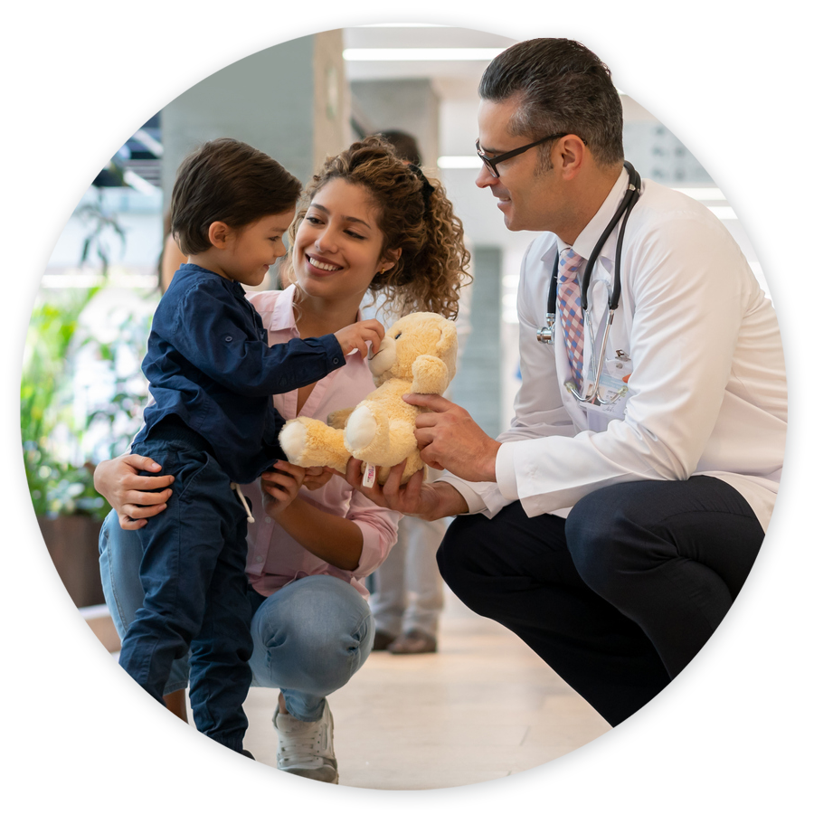 Doctor giving child a stuffed animal in the halls of a children's hospital with his mom