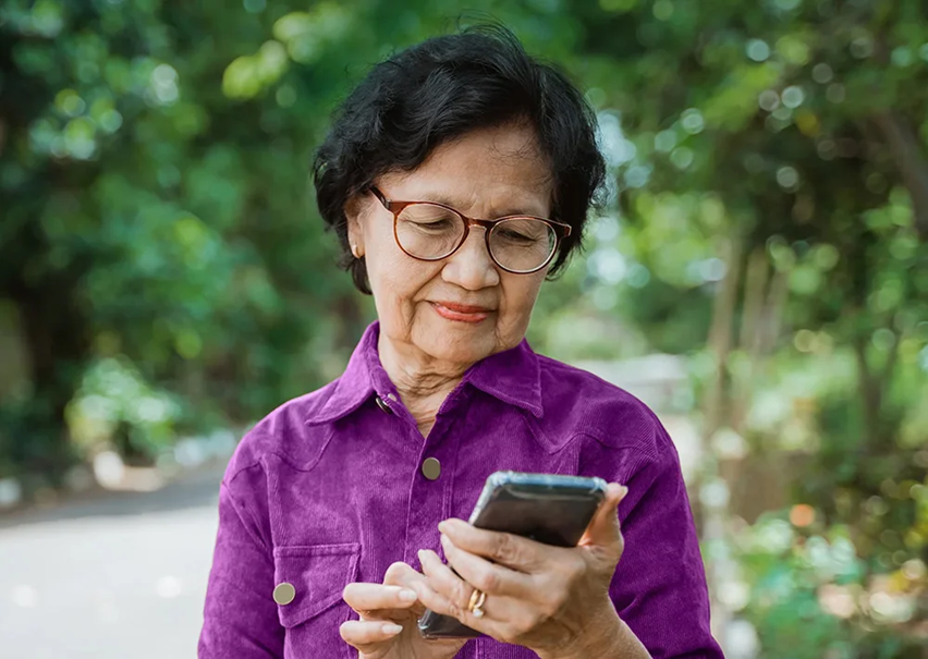 a photo of an older woman smiling while using a cell phone