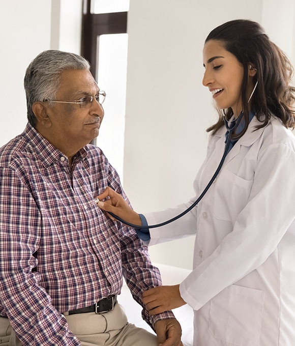 Female doctor checking middle-aged male patient's heart with stethoscope