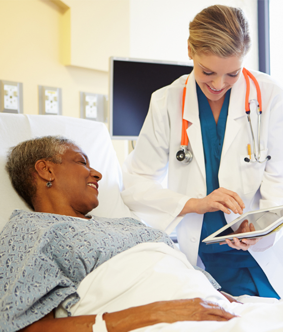 Female doctor smiling showing patient in hospital bed results on tablet