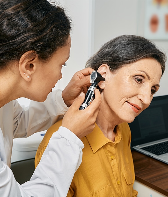 Female doctor using otoscope to look in ear of middle-aged female patient