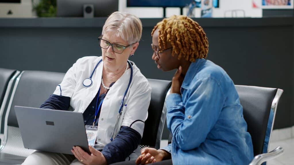 Female doctor with stethoscope showing laptop screen to female patient during medical consultation in healthcare office setting