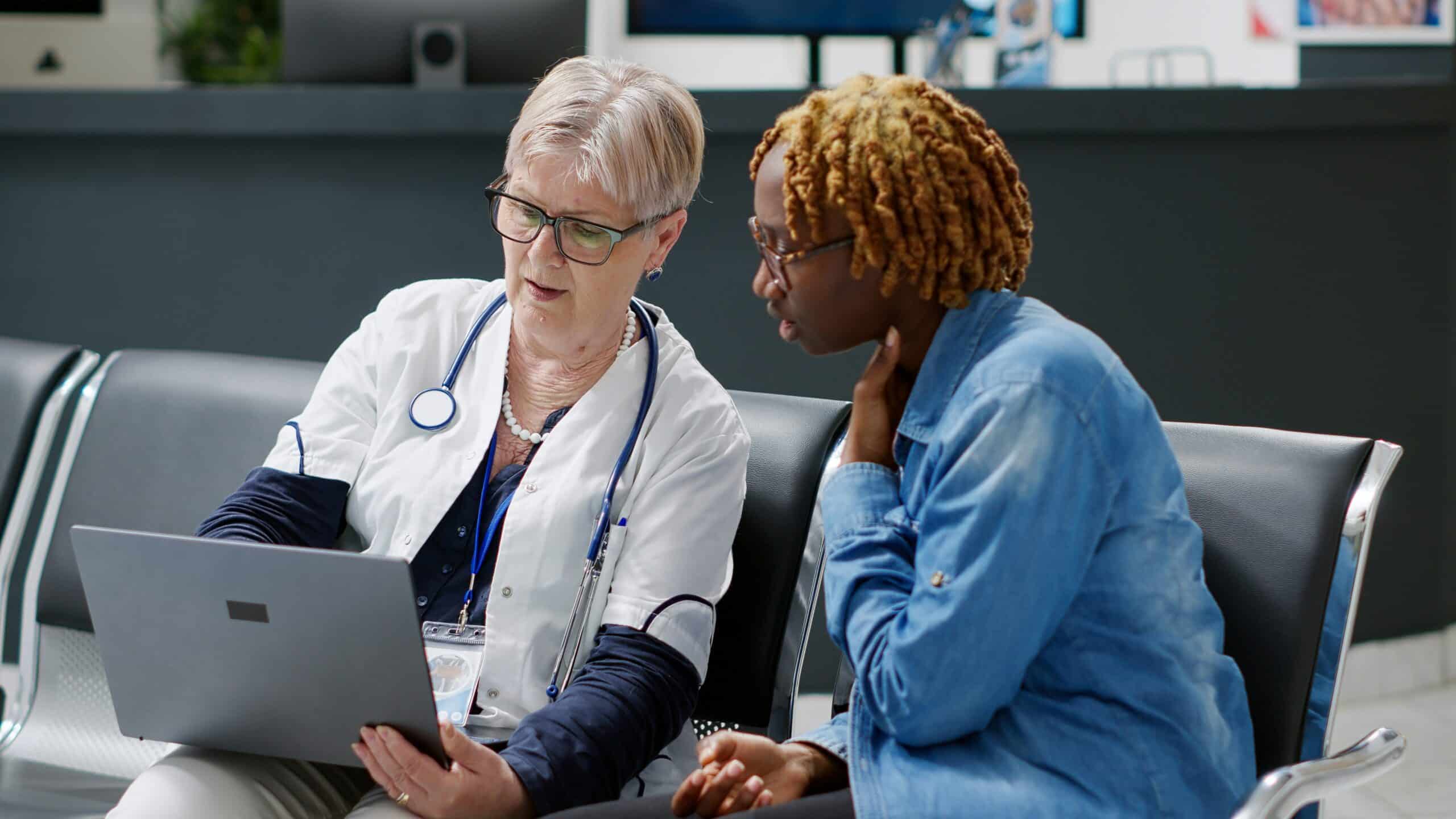 Female doctor with stethoscope showing laptop screen to female patient during medical consultation in healthcare office setting