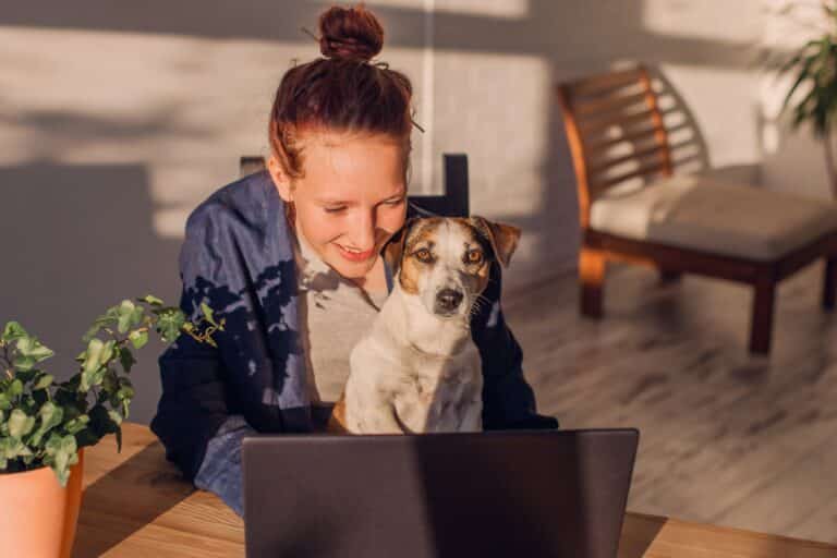 young woman smiling with dog on lap at table with laptop